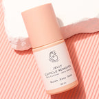 A 30 ml bottle of GEL WITH US Jelly Cuticle Remover, featuring a light peach-pink cap and a white label with black text, styled on a pink striped background with a white textured stone prop.