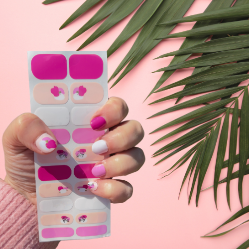 Hand wearing Pink Silhouette berry and blush flower nail polish wraps beside a palm leaf