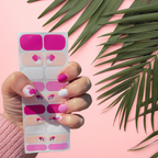 Hand wearing Pink Silhouette berry and blush flower nail polish wraps beside a palm leaf